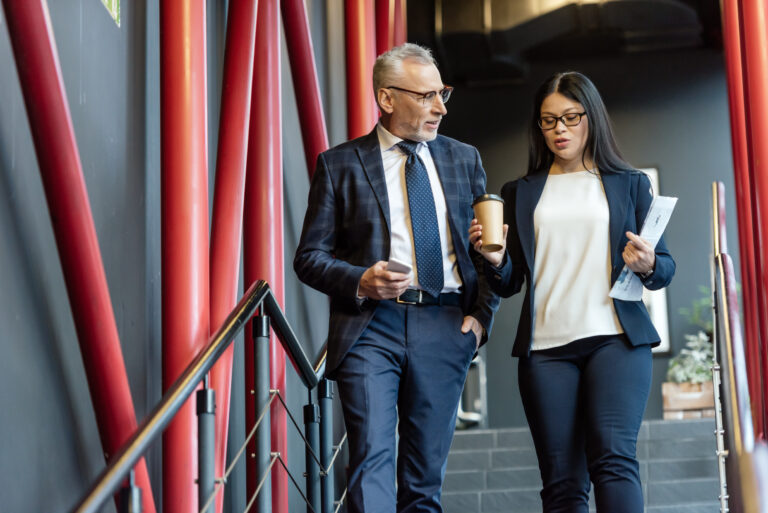 businessman with smartphone and asian businesswoman with paper cup talking and walking on stairs